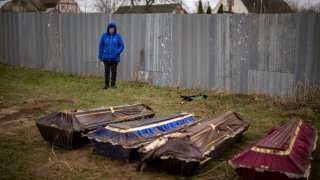 Ira Slepchenko, 54, stands next to coffins, one of them with the body of her husband Sasha Nedolezhko, 43, during an exhumation of a mass grave in Mykulychi, Ukraine on Sunday, April 17, 2022.