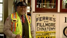 Cable Car gripman Valentine Lupiz stands in front of historic car Big 19 in SFMTA's cable car barn.