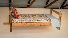 a twin bed with kids' sheets and pillows, hangs on display in a barn.