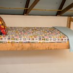 a twin bed with kids' sheets and pillows, hangs on display in a barn.