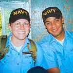 Two U.S. Navy recruits in light blue uniform shirts, wearing caps that say "Navy" on them.