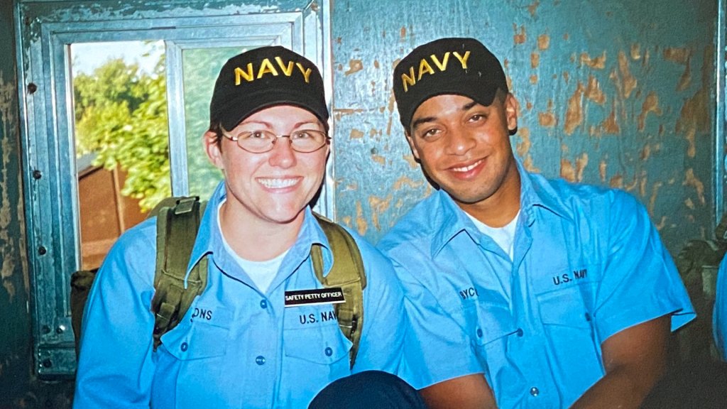 Two U.S. Navy recruits in light blue uniform shirts, wearing caps that say "Navy" on them.