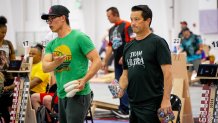 two men in cornhole-themed T-shirts get ready to throw bean bags