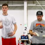 A man on the left throws a bean bag. A man on the right gets ready to throw.