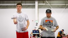 A man on the left throws a bean bag. A man on the right gets ready to throw.