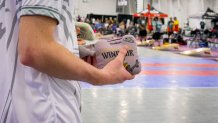 a hand holds a purple cornhole bag that says "windsor" on it.