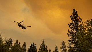 A helicopter flies through a smoky sky to make a water drop at the Oak Fire.