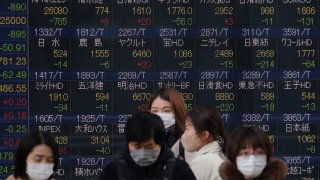 Pedestrians walk in front of an electronic quotation board displaying stock prices of the Tokyo Stock Exchange in Tokyo on March 7, 2022.