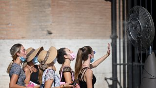 TOPSHOT – A group of woman cool off in front of a cooling fan during a heatwave as they queue at the enterance of the Colosseum in Rome on August 12, 2021. – An anticyclone dubbed Lucifer is sweeping across Italy, sending temperatures soaring and causing what is believed to be a new European record of 48.8 degrees Celsius (119.8 Fahrenheit) in Sicily on August 11. (Photo by Alberto PIZZOLI / AFP) (Photo by ALBERTO PIZZOLI/AFP via Getty Images)