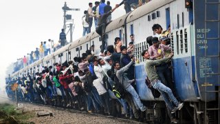 Indian passengers stand and hang onto a train as it departs from a station on the outskirts of New Delhi.