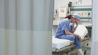 View through privacy curtains to female doctor sitting with head in hand