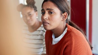 Emotionally stressed young woman crying while looking away sitting with friend during psychotherapy in classroom at university