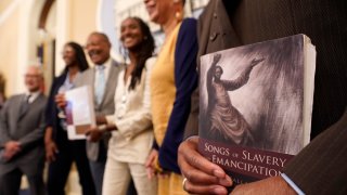 Dr. Amos C. Brown, Jr., vice chair for the California Reparations Task Force, right, holds a copy of the book Songs of Slavery and Emancipation, as he and other members of the task force pose for photos at the Capitol in Sacramento, Calif., on June 16, 2022.