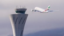 An Emirates A380 takes off into the fog at San Francisco International Airport, flying past the airport's control tower.