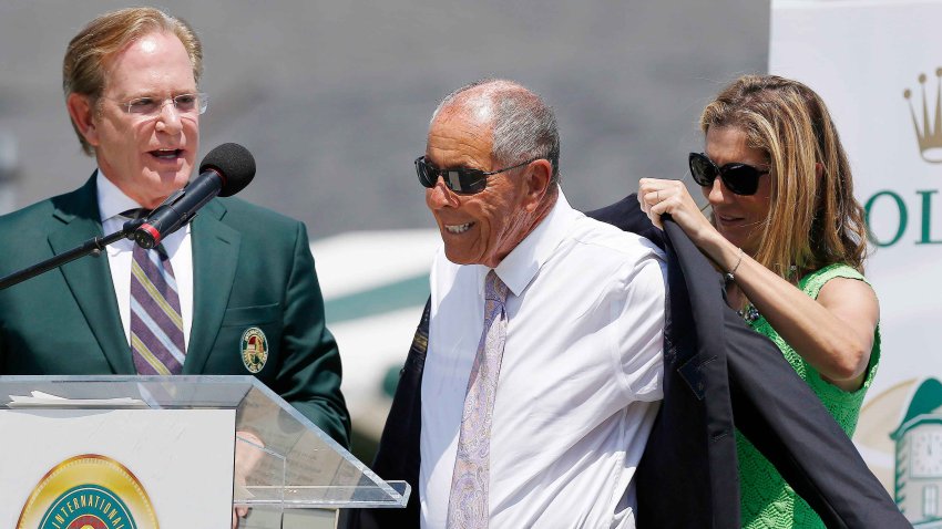 Monica Seles, right, helps Nick Bollettieri with a blazer as Hall of Fame chairman of the board Christopher Clouser, left, looks on during Bollettieri’s induction into the International Tennis Hall of Fame in Newport, R.I., Saturday, July 12, 2014.