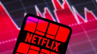 In this photo illustration the Netflix logo seen displayed on a smartphone screen, with graphic representation of the stock market in the background.