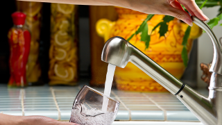 A person using a faucet to fill a glass with water.