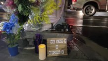 Flowers left at an intersection alongside a lit candle and a sign that says "WE LOVE U BROOKE."