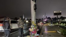 The intersection of Stoneman Avenue and Briarcliff Drive in Pittsburg at night, with two people standing in the left side of the photo near the street. At the base of the pole in the center of the photo, people have placed flowers and candles to memorialize 17-year-old Brooke Jeffrey who died there.