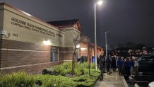 A brick school building with bushes in front of it is pictured at night. On the right side of the photo, dozens of people are gathered together for a memorial for 17-year-old Brooke Jeffrey.