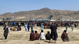 FILE – Hundreds of people gather near a U.S. Air Force C-17 transport plane at the perimeter of the international airport in Kabul, Afghanistan, Aug. 16, 2021.