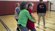 A volunteer instructor from Asians Are Strong watches as a pair of seniors practice an exercise aimed at breaking the grip of an attacker.
