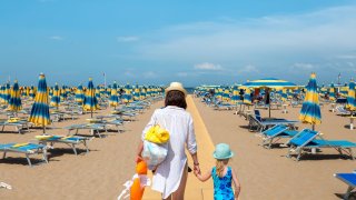 Woman and child outdoors. Mother and daughter going to rest on beach. Rimini, Italy.