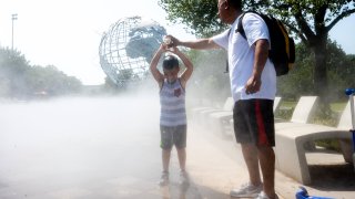 Samio, 8, and his father, pour water on each other to cool off while playing in cooling mist near the Unisphere in Flushing Meadows Corona Park as temperatures reach above 90 degrees on August 12, 2021 in the Queens Borough of New York City. New York City is experiencing a heat wave with a heat index of 100+ causing extreme temperatures, humidity and possible storms.