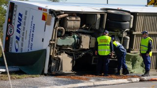 Police inspect underneath a bus that rolled onto its side near Greta in the Hunter Valley, north of Sydney, Australia, Monday, June 12, 2023.