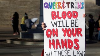 FILE – A protester outside the Kansas Statehouse holds a sign after a rally for transgender rights on the Transgender Day of Visibility, Friday, March 31, 2023, in Topeka, Kansas.