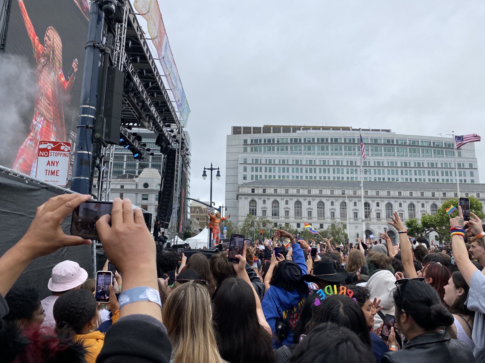Hayley Kiyoko performs on a stage in San Francisco at the Pride Celebrations in an orange outfit while onlookers hold up their cell phones