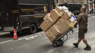 United Parcel Service (UPS) driver pushes a dolly of packages towards a delivery van on a street in New York.