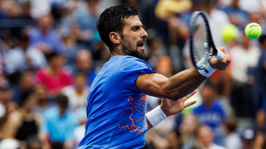 Novak Djokovic in blue shirt hits tennis ball