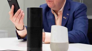FILE - A man holds an iPhone next to an Amazon Echo, center, and a Google Home, right, in New York on June 14, 2018.