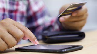 Closeup young man hands holding credit card and using cell, smart phone for online shopping or reporting lost card, fraudulent transaction