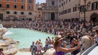 A woman takes a selfie with an ice cream cone in front of Rome's Trevi Fountain.