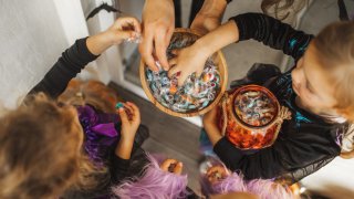 Children happy to receive many sweets and gifts. All girls wearing in bright witch of fairy dresses. Happy childhood. American traditional culture of Halloween celebration. Top view, copy space background with unrecognizable people.