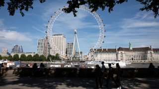 Tourists walk in silhouette across the river from the London Eye, one of the most famous landmarks, skylines and iconic buildings in the capital in London, England, United Kingdom.