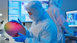 A technician holds a semiconductor wafer at a manufacturing plant.