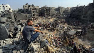 A man sits on the rubble as others wander among debris of buildings that were targeted by Israeli airstrikes in Jabaliya refugee camp, northern Gaza Strip, Wednesday, Nov. 1, 2023.