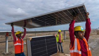 Workers carry a solar panel for installation at the under-construction Adani Green Energy Limited's Renewable Energy Park
