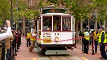 The white front of a cable car with the number 19 painted on it prepares to break through a pink polka-dotted ribbon at the start of its run.