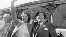 Black and white photo with a young mayor Dianne Feinstein on the left and a young Tony Bennett on the right, waving from the running board of a cable car, both wearing berets bearing the Muni logo.