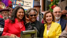 Mayor London Breed dressed in red, and U.S. Rep. Nancy Pelosi, dressed in yellow, stand on either side of Fannie Mae Barnes, dressed in black and wearing sunglasses, posing for a photo at a crowded public outdoor event.