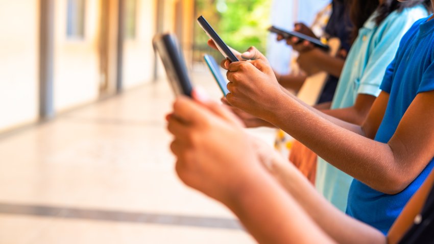 Close up shot, group of children hands busy using smartphone at school corridor - concept of social media, playing games, technology and education