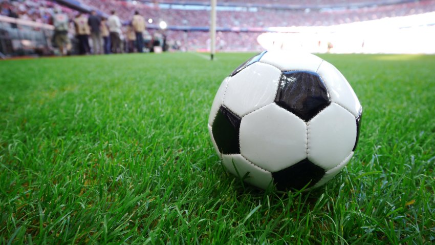 Soccer ball on grass field blur people in stadium.