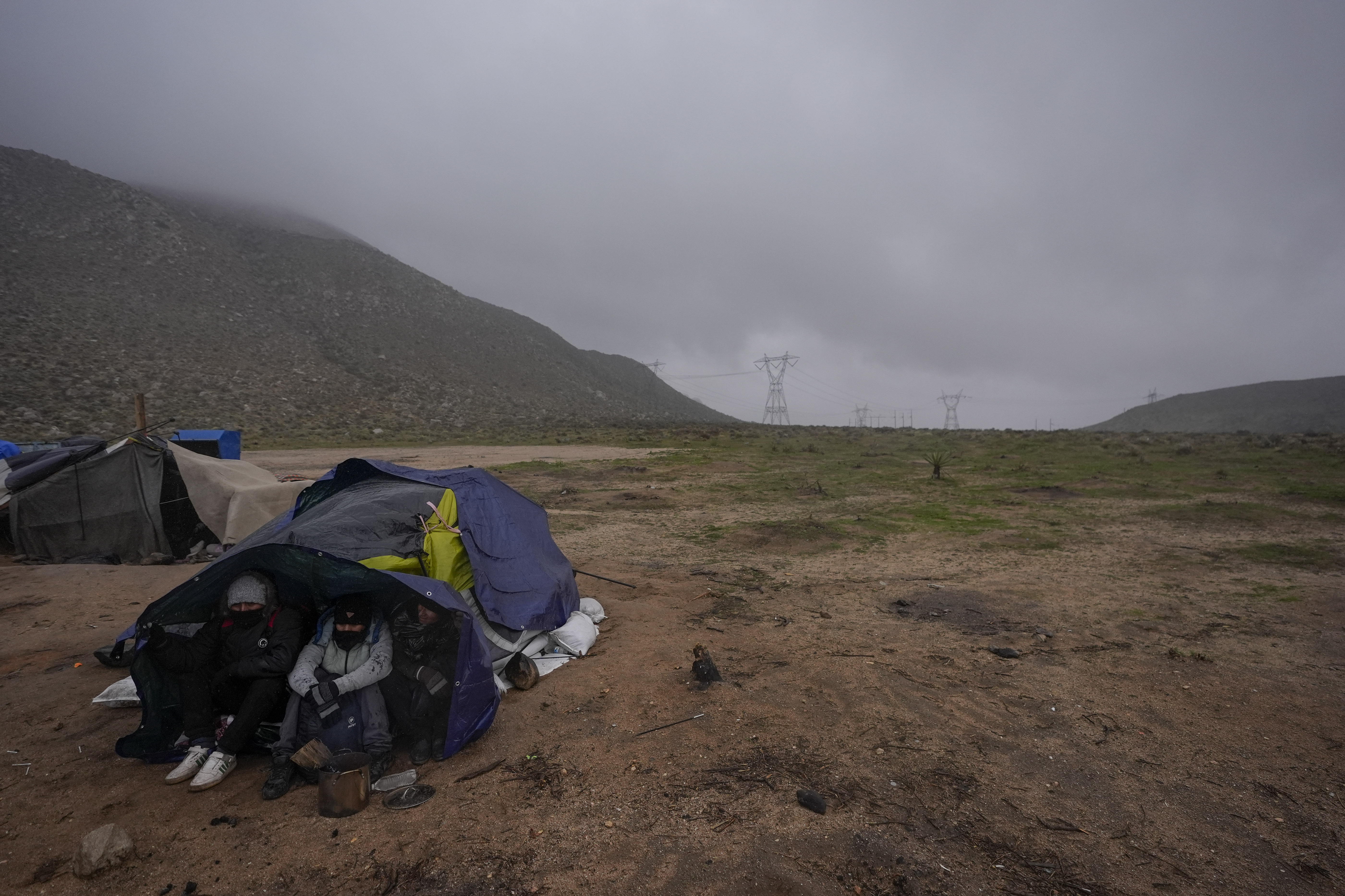 Migrants seeking asylum from Ecuador take shelter from wind and rain as they await processing in a makeshift, mountainous campsite after crossing the border between Mexico and the United States, Friday, Feb. 2, 2024, near Jacumba, Calif. About 200 migrants huddled under blankets and plastic bags under pounding rain and wind Friday night, as Border Patrol agents tried to work out transportation to area facilities.