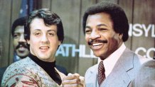 American actors Sylvester Stallone (L) and Carl Weathers grip hands and smile together during a press conference in a still from the film, 'Rocky,' directed by John G. Avildsen, 1976. (Photo by United Artists/Courtesy of Getty Images)