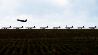 A plane takes off as others are parked on a runway at Denver International Airport