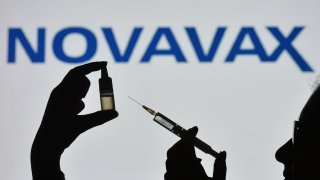 In this photo illustration a silhouette of a man holding a medical syringe and a vial seen displayed in front of the Novavax logo on a screen.